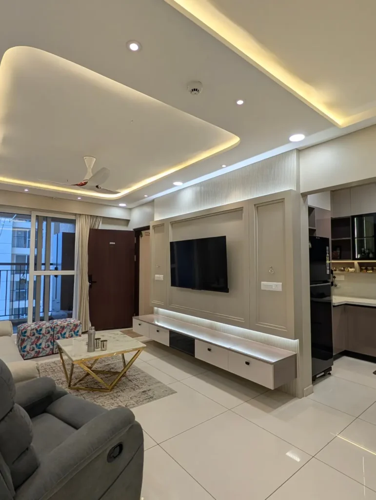 Completed 3 BHK living room in Bengaluru with panelled TV wall, fluted backdrop, floating TV unit with LED lighting and cove-lit false ceiling by Aladi Interiors