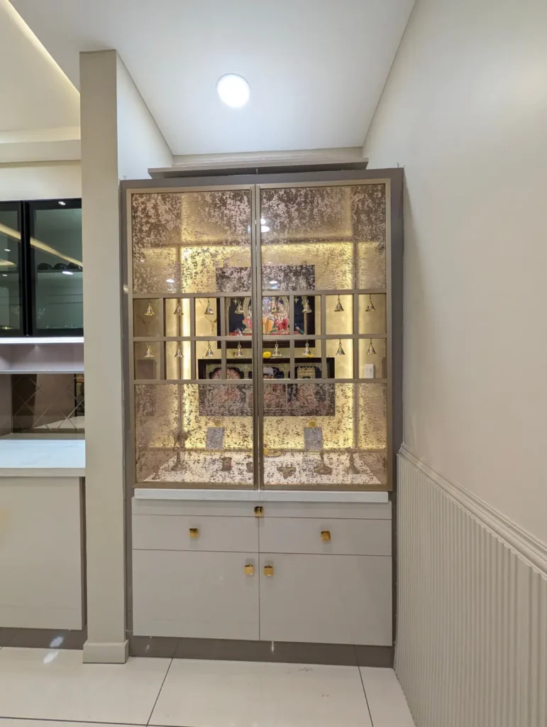 Completed pooja unit in a Bengaluru 3 BHK with textured glass doors, gold frame, brass bells and backlit onyx panel by Aladi Interiors
