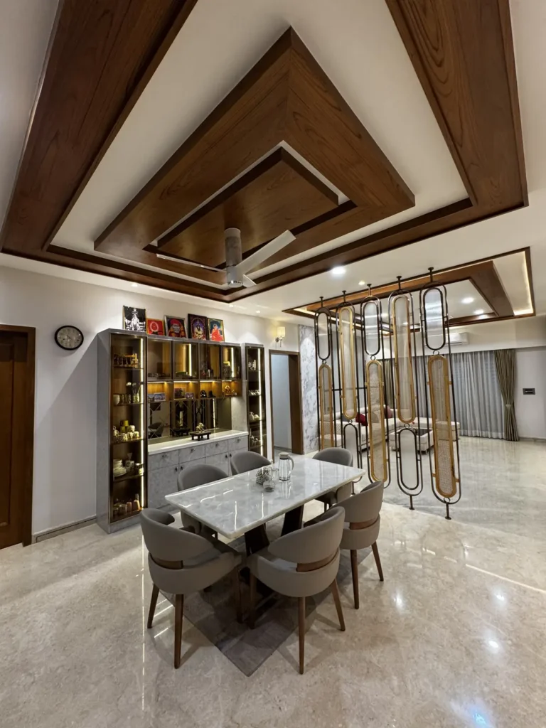 Dining area with marble-top dining table, glass crockery unit, decorative partition and wooden false ceiling in a Gulbarga 3 BHK by Aladi Interiors
