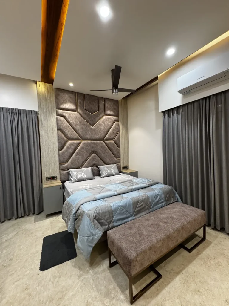 Master bedroom with geometric upholstered headboard wall, bench and warm false ceiling lighting in a Gulbarga 3 BHK by Aladi Interiors